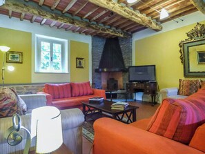 A cozy living room with a fireplace, a sofa, a television, and a stone wall. - Historic villa with pool and tennis near Lucca (San Ginese)