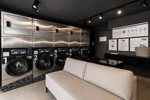 Eine moderne Waschküche mit mehreren Waschmaschinen, einer Couch und Informationsplakaten an der Wand.