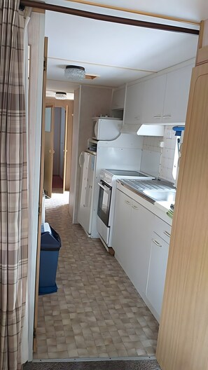 Eine schmale Küche mit weißen Schränken, einem Kühlschrank und einer Mikrowelle.
