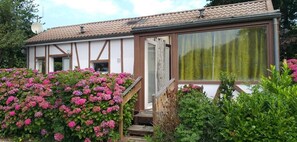 A building with a white exterior and brown trim, featuring a large window and a door. - Chalet 'Bungalow Chouette' with Private Terrace and Private Garden (Néville)