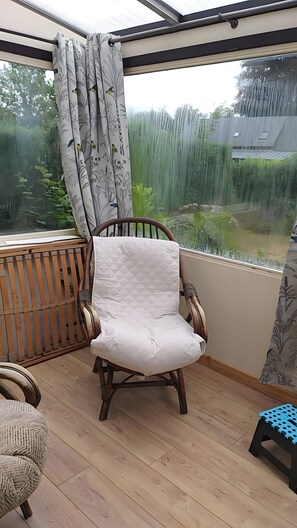 A room with a wooden floor, a cushioned chair, a small stool, and a window with a curtain.