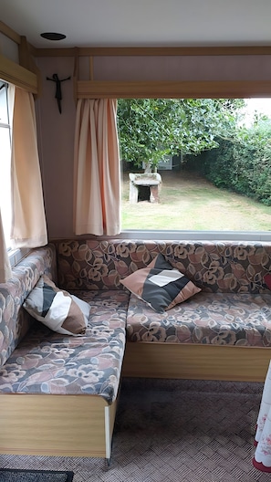 A cozy interior with a cushioned bench, a window with curtains, and a view of a garden. - Chalet 'Bungalow Chouette' with Private Terrace and Private Garden (Néville)