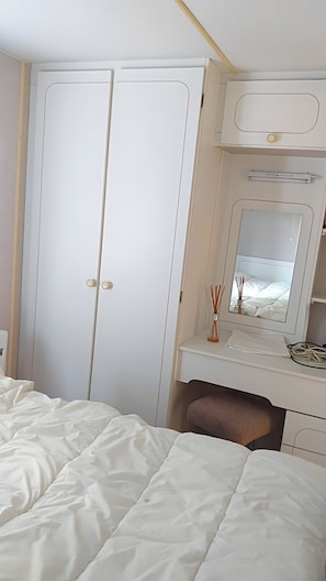 Ein Schlafzimmer mit einem Bett, einem Kleiderschrank, einem Schreibtisch mit Spiegel und einem Nachttisch.