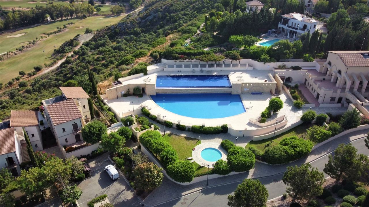 A large swimming pool surrounded by a landscaped garden, with a golf course in the background.