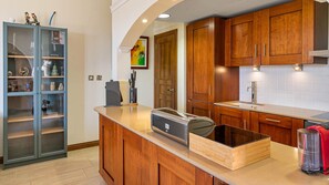 A modern kitchen with wooden cabinets, a built-in island, and a glass-fronted cabinet with decorative items. - Apartment APINAGA - Jakarta (Kouklia)