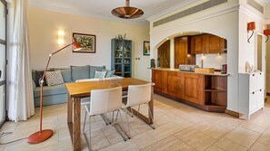 Eine moderne Küche mit Holzausstattung, ein Essbereich mit Holztisch und -stühlen sowie ein Wohnzimmer mit Sofa und Stehlampe.