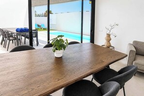 A conference room with a wooden table, chairs, a potted plant, and a view of a swimming pool. - Casa Drago Uno - Three Bedroom Villa, Sleeps 5 (Caleta de Fustes)