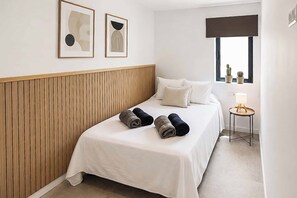 Habitación de hotel con cama, almohadas, mesita de noche con lámpara y dos cuadros en la pared.