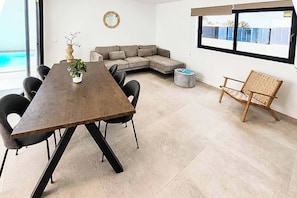 A modern interior with a wooden dining table, black chairs, a grey sofa, a small round table, and a wicker chair. - Casa Drago Uno - Three Bedroom Villa, Sleeps 5 (Caleta de Fustes)