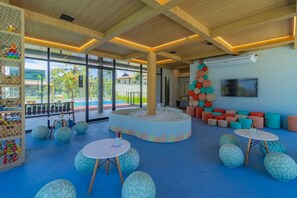 A modern indoor space with a central seating area, a large window, and a TV on the wall. - Cais Eco #110 - Seaside Resort by Carpediem (Ipojuca)