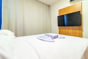 A hotel room with a bed, a flat-screen TV mounted on a wooden panel, and a window with curtains. - Cais Eco #110 - Seaside Resort by Carpediem (Ipojuca)