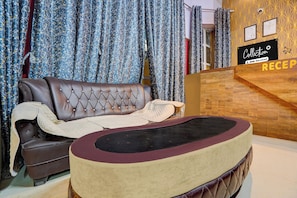 A reception area with a wooden reception desk, a brown leather sofa, and a patterned curtain backdrop. - Collection O Patna Airport Road (Danapur)