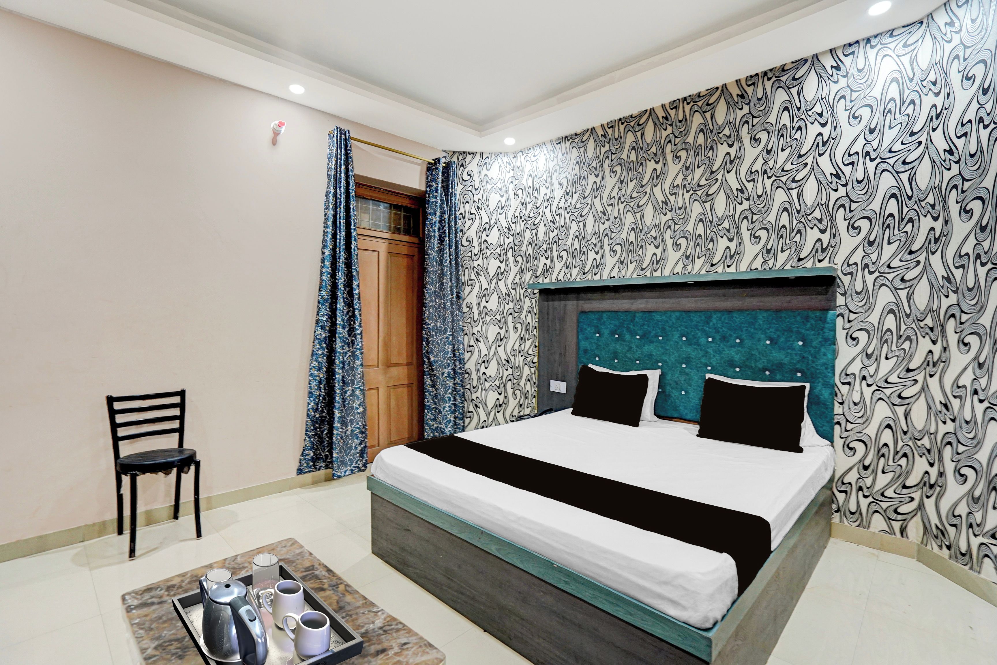 Quarto de hotel com uma cama, uma cadeira e um tabuleiro com chaleira e xícaras.