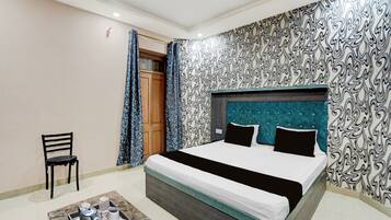 Quarto de hotel com uma cama, uma cadeira e um tabuleiro com chaleira e xícaras.