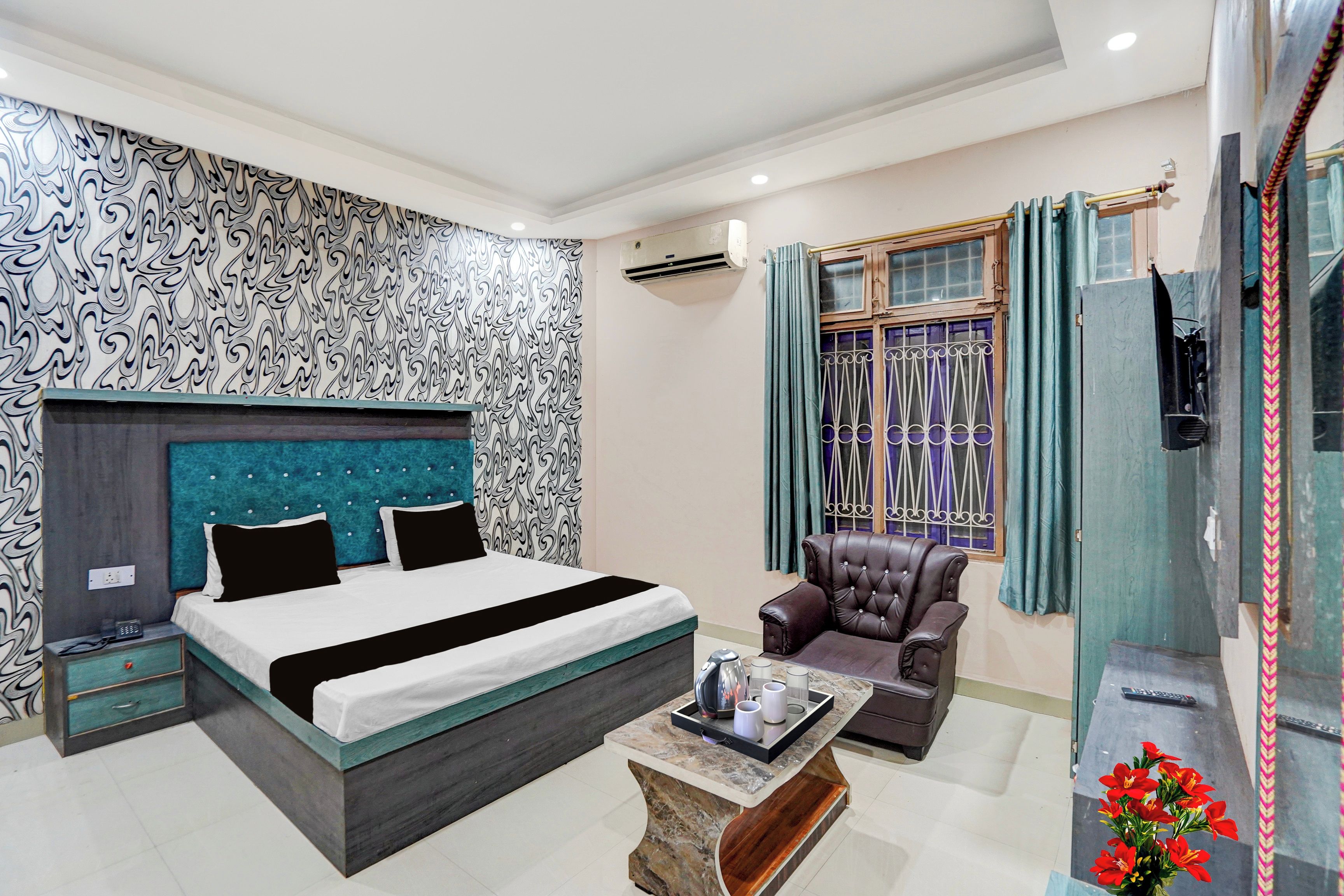Quarto de hotel moderno com cama, área de estar, mesinha e janela com cortinas.