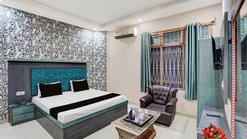 Quarto de hotel moderno com cama, área de estar, mesinha e janela com cortinas.