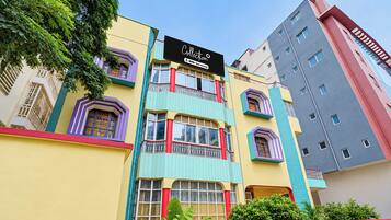 Um edifício de vários andares com fachada colorida, apresentando varandas com grades ornamentadas, janelas amplas e uma placa indicando uma área de serviço.