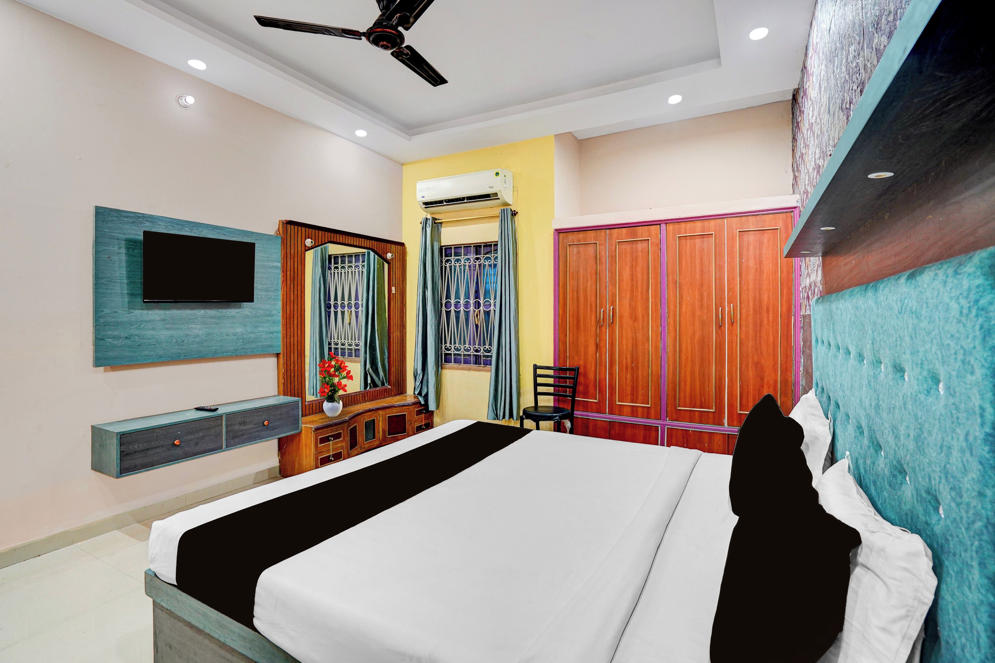 A bedroom with a bed, a TV, a wardrobe, a ceiling fan, and an air conditioning unit.