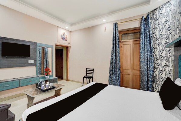 A hotel room with a bed, a TV mounted on the wall, a desk with a mirror, a chair, and a window with curtains. - Collection O Patna Airport Road (Danapur)