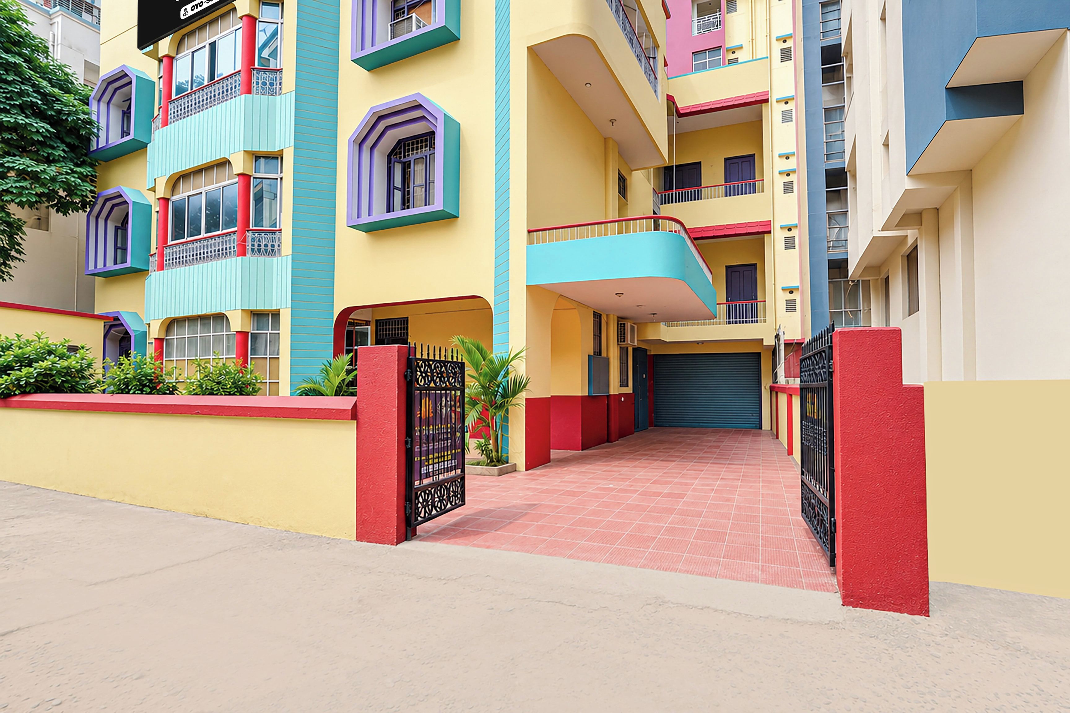 A multi-story residential building with a red and yellow facade, balconies, and a gated entrance.