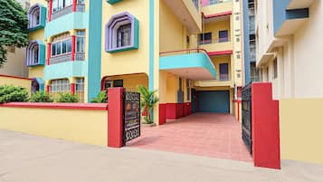 A multi-story residential building with a red and yellow facade, balconies, and a gated entrance.