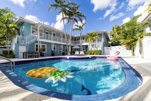 A hotel with a swimming pool, palm trees, and a two-story building with balconies. - La Casa Verde 1 | 1 Bedroom Coral Ridge Apt w/Pool (Fort Lauderdale)