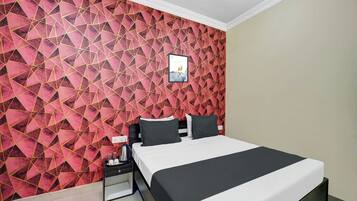 Une chambre d’hôtel avec un mur orné d’un motif géométrique, un lit avec une literie noire et blanche, une table de chevet avec une bouilloire et un tableau encadré accroché au mur.