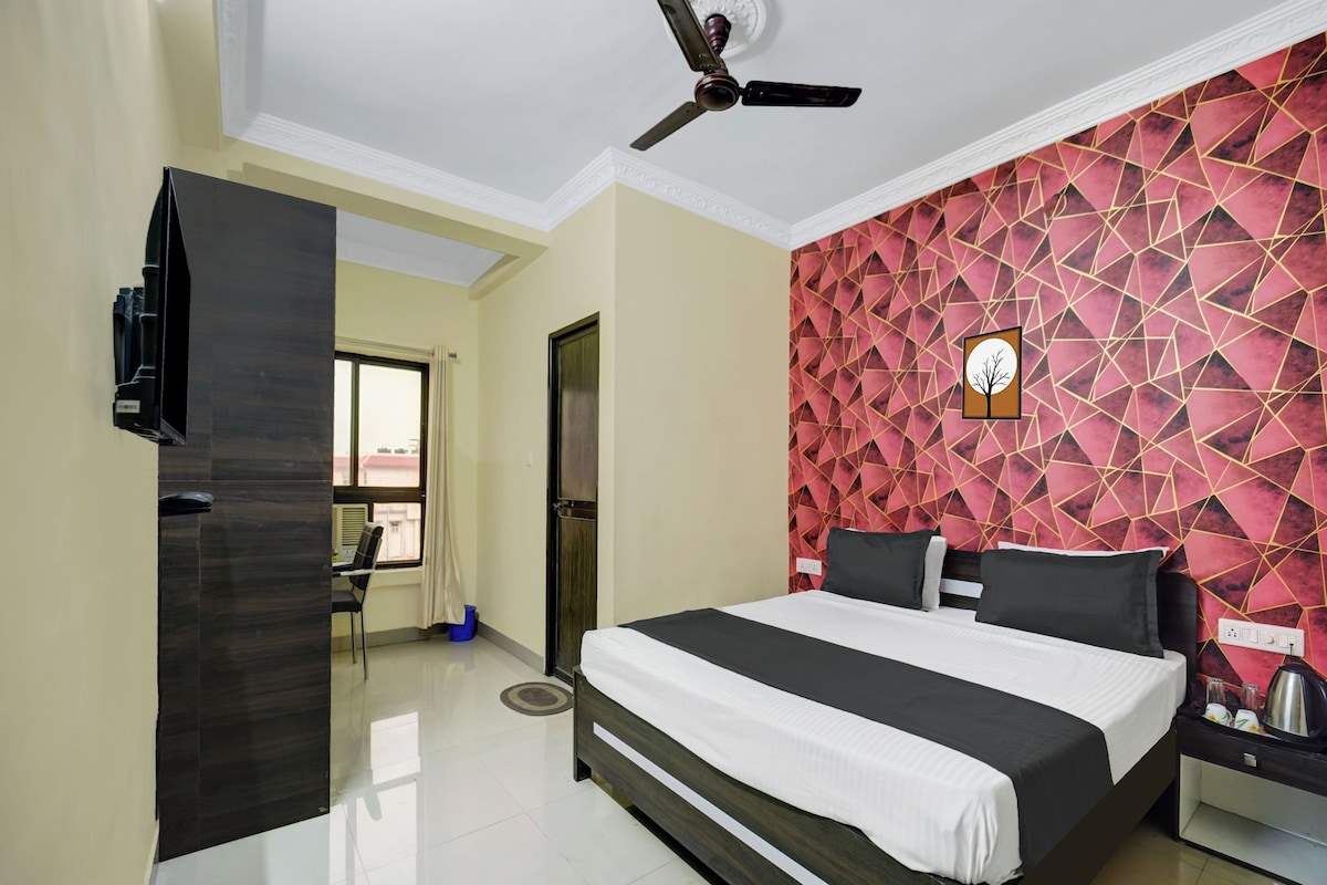 A hotel room with a bed, a ceiling fan, a TV, and a red geometric-patterned wall.