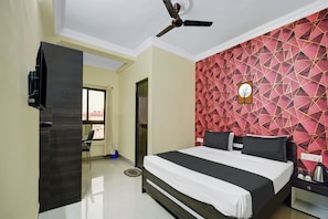 A hotel room with a bed, a ceiling fan, a TV, and a red geometric-patterned wall. - Collection O Patliputra Station (Danapur)