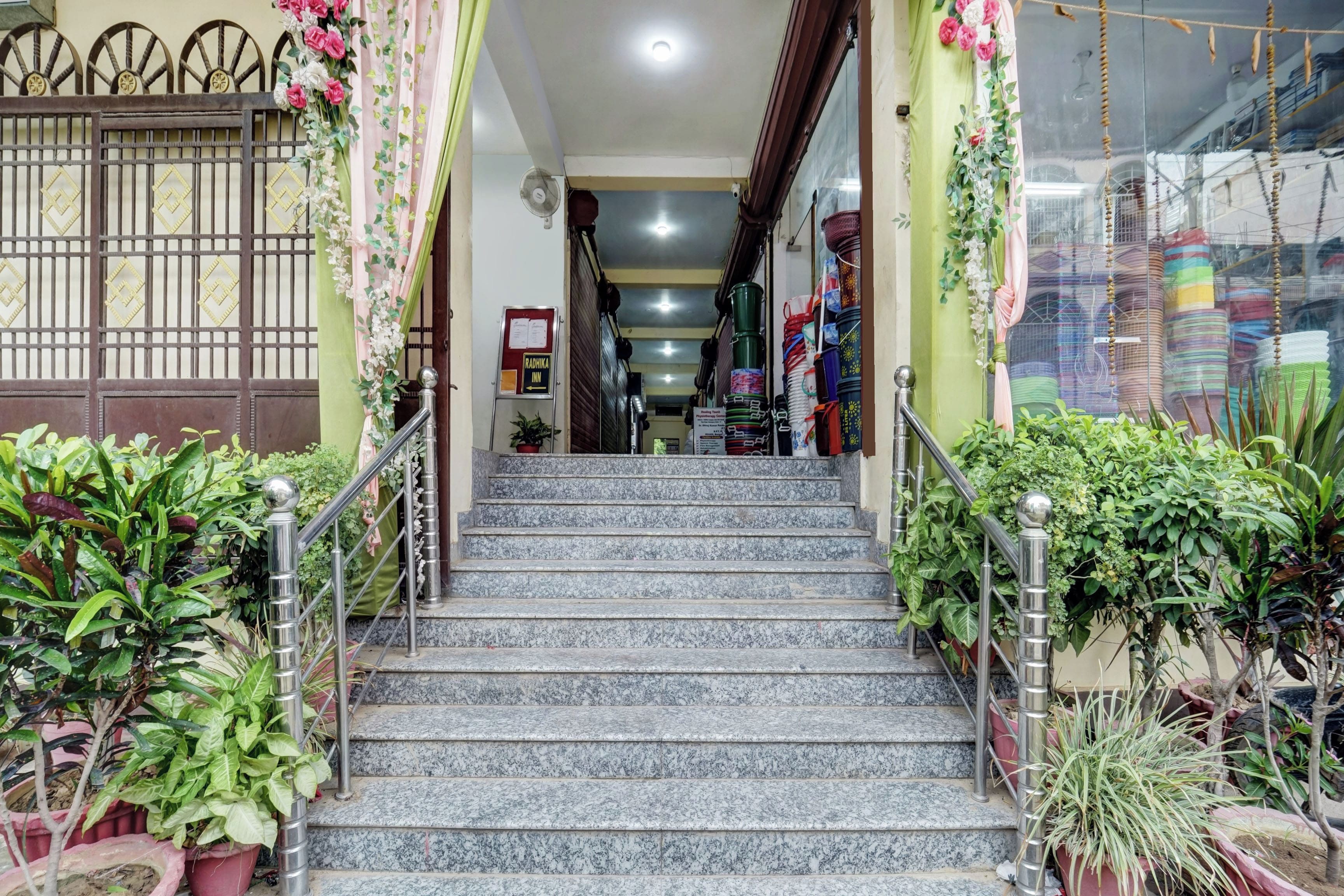 Una escalera conduce a la entrada de un hotel, con un letrero que dice 'Radhika Inn' y vistas del interior.