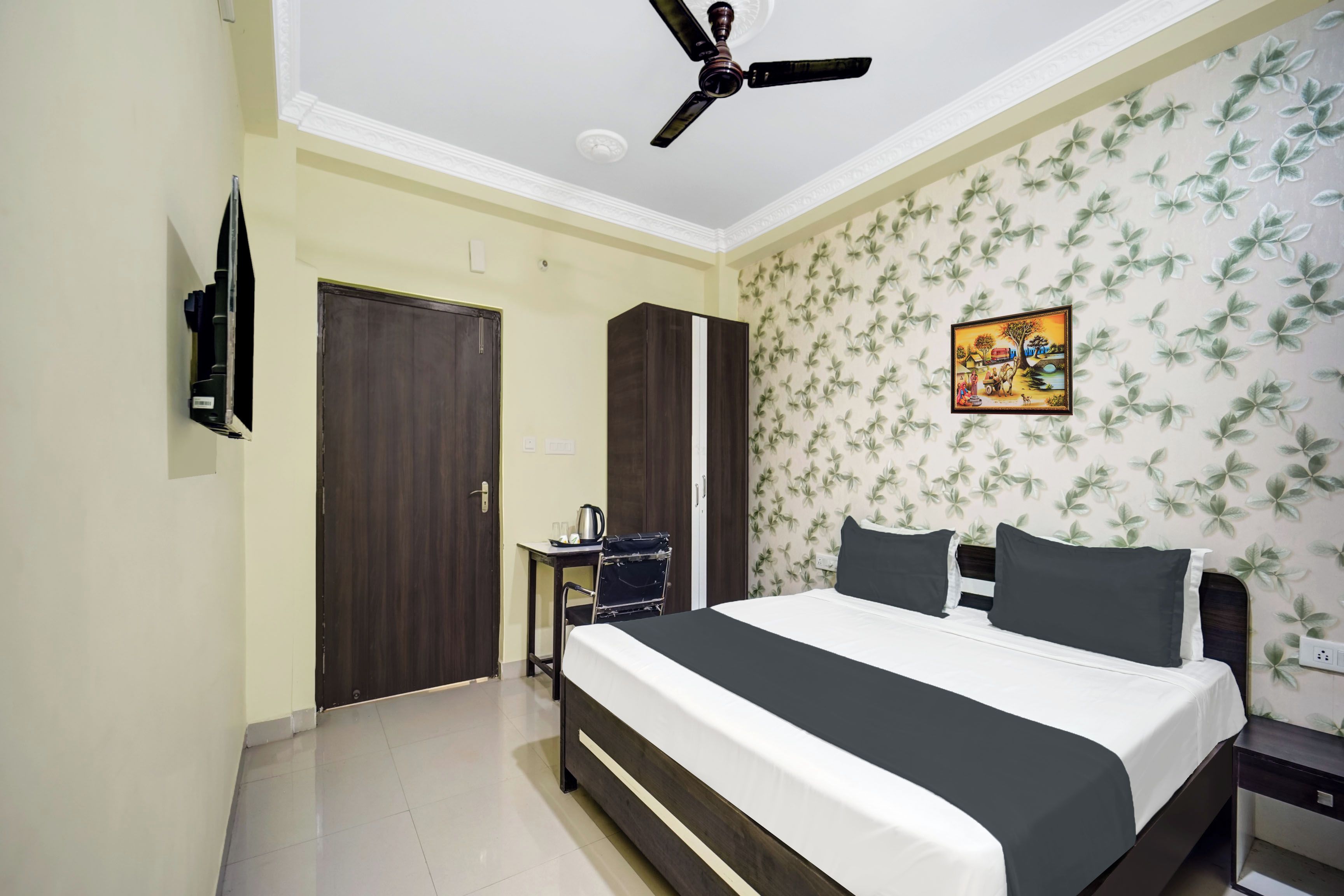 Un dormitorio con cama, ventilador de techo, armario, escritorio con silla y pared con estampado floral.