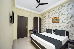 A bedroom with a bed, a ceiling fan, a wardrobe, a desk with a chair, and a wall with a floral pattern. - Collection O Patliputra Station (Danapur)