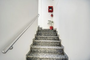 A staircase with a metal handrail, a red fire alarm, and a potted plant. - Collection O Patliputra Station (Danapur)