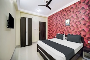 A bedroom with a bed, a ceiling fan, a TV mounted on the wall, and a geometric-patterned wall. - Collection O Patliputra Station (Danapur)