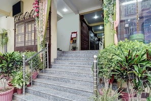 A staircase leading to a building entrance with a metal railing, surrounded by potted plants. - Collection O Patliputra Station (Danapur)