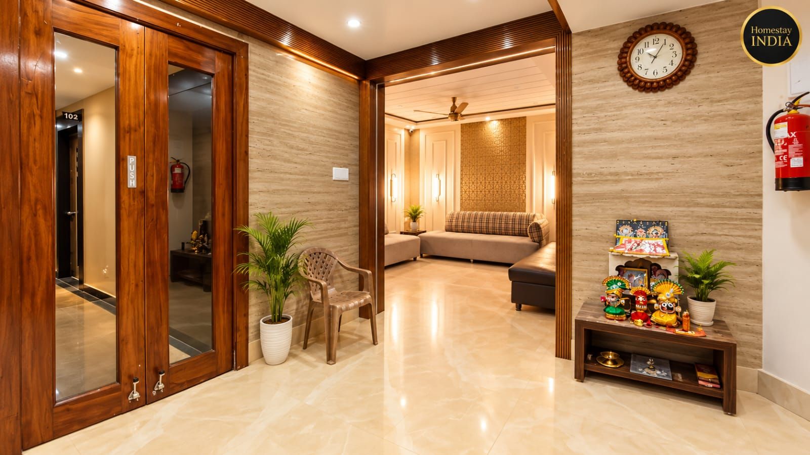 A hotel lobby with a wooden reception desk, a seating area with a sofa and armchairs, a wall-mounted clock, and a shelf with decorative items.