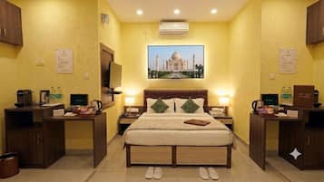 A hotel room with a bed, bedside tables, a television, and a picture of the Taj Mahal on the wall.