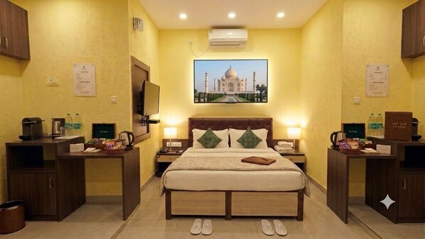 A hotel room with a bed, bedside tables, a television, and a picture of the Taj Mahal on the wall.