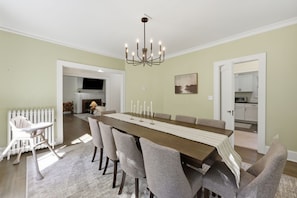 A dining area with a long table, multiple chairs, a chandelier, a fireplace, and a kitchen visible through an open door. - Spacious Shaker Heights Retreat  Sleeps 10 (Shaker Heights)
