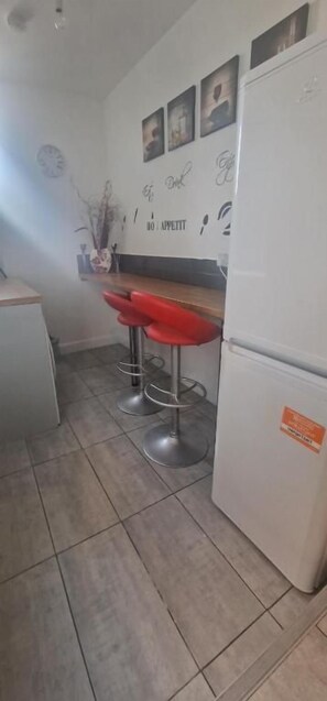 A kitchen with a white refrigerator, a clock, and a wall with framed pictures and a sign. - Single & Double rooms in Stoke on trent (Stoke-on-Trent)