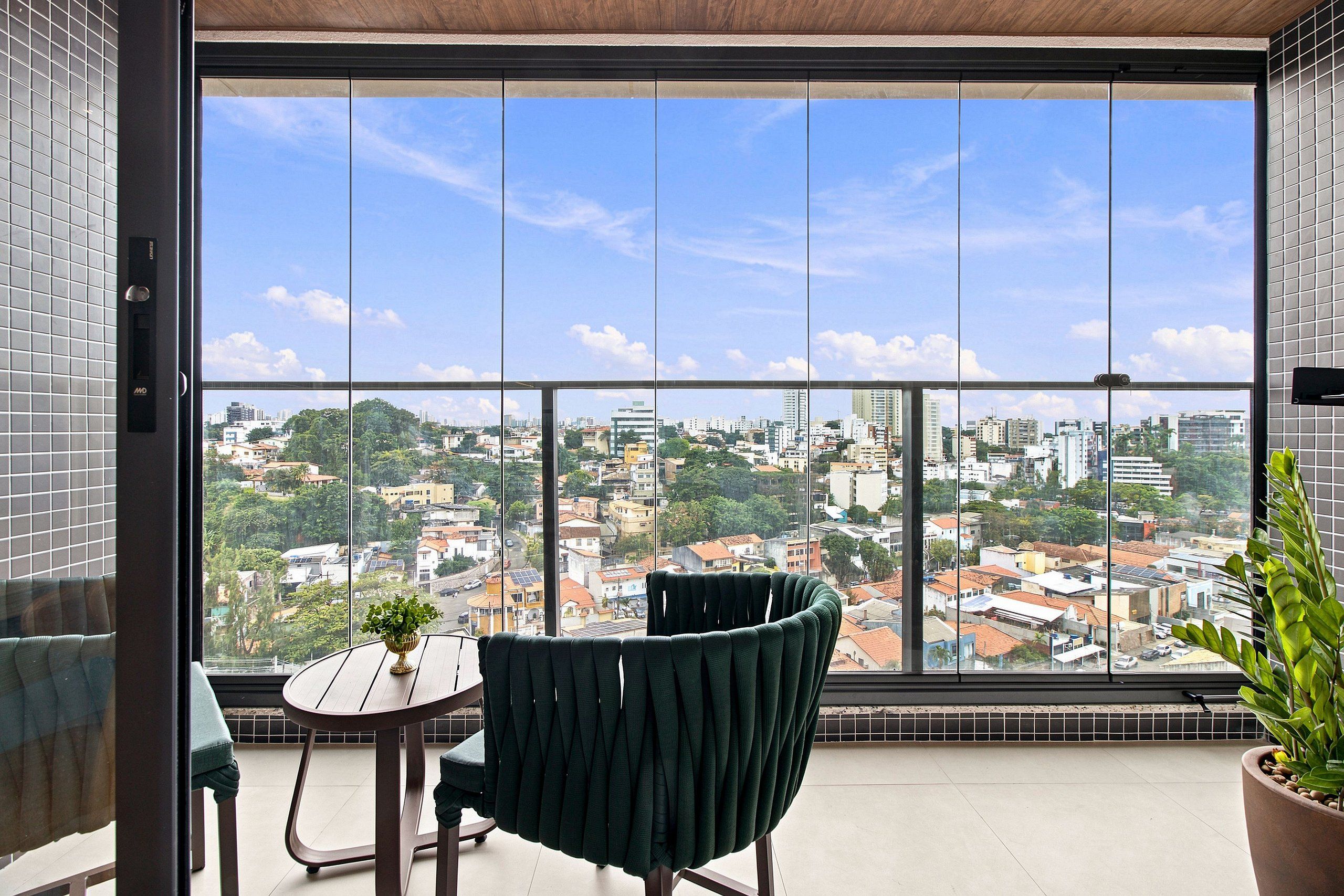 A balcony with a view of a cityscape, a chair, a small table, and a potted plant.