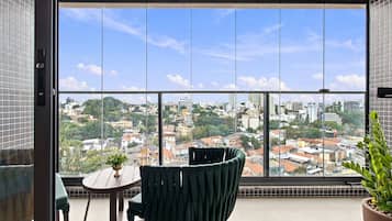 A balcony with a view of a cityscape, a chair, a small table, and a potted plant.