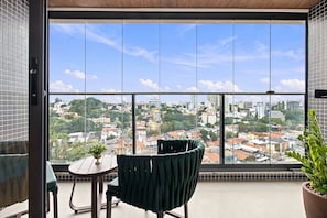 A balcony with a view of a cityscape, a chair, a small table, and a potted plant. - Beach Class Rio Vermelho Salvador Near Barra and Ondina by Carpediem (Salvador)