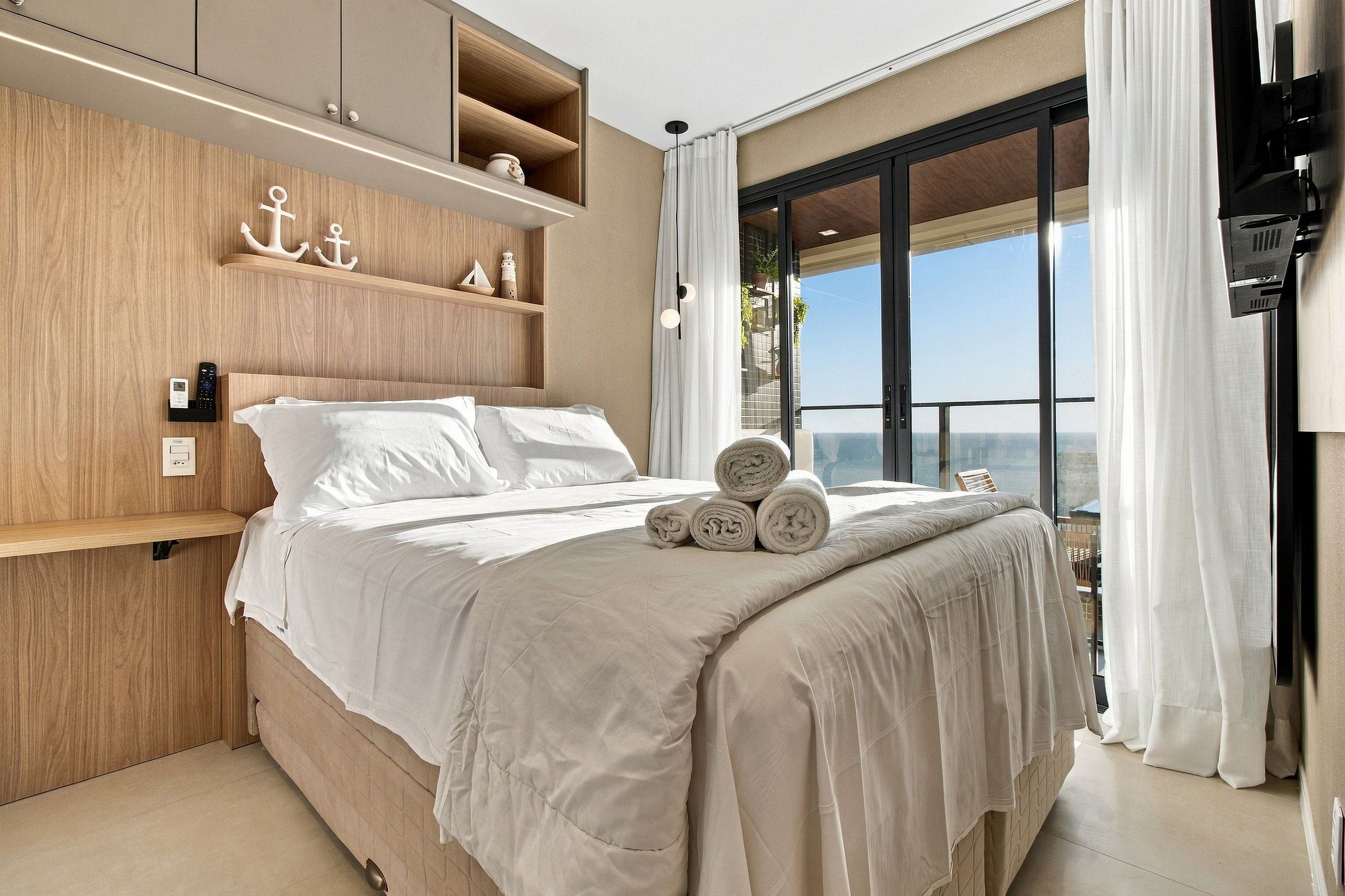 A bedroom with a bed, a wooden headboard, a window with curtains, and a view of the outside.