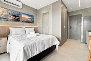 A modern bedroom with a large bed, a nightstand, a wardrobe, and a door leading to a bathroom. - Beach Class Rio Vermelho Salvador Near Barra and Ondina by Carpediem (Salvador)