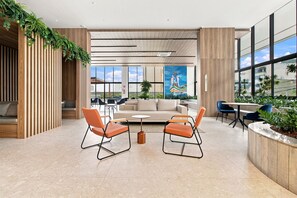 A modern interior with a sofa, two orange chairs, a coffee table, and a large window with a view. - Beach Class Rio Vermelho Salvador Near Barra and Ondina by Carpediem (Salvador)