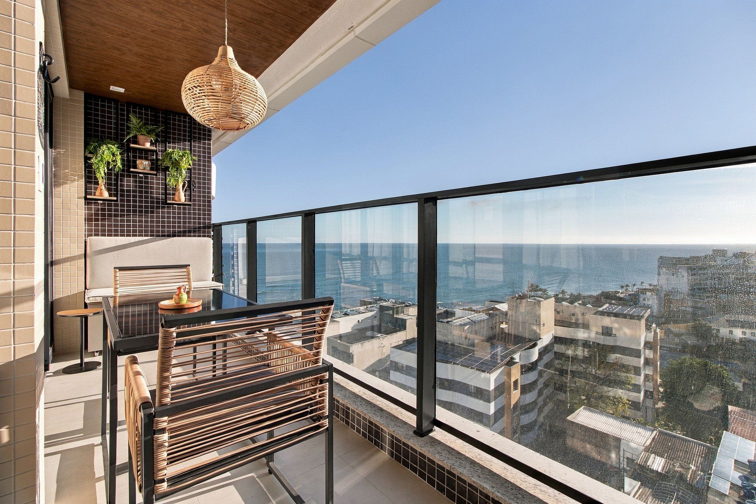 A balcony with a view of the city and the sea, a hanging light fixture, and potted plants.