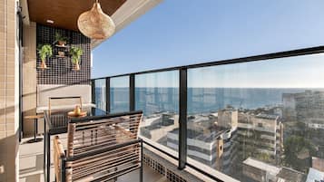 A balcony with a view of the city and the sea, a hanging light fixture, and potted plants.