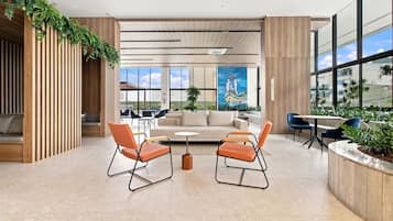 A modern interior with a sofa, two orange chairs, a coffee table, and a large window with a view.