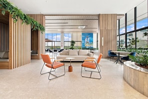 A modern interior with a sofa, two orange chairs, a coffee table, and a large window with a view. - Beach Class Rio Vermelho Salvador Near Barra and Ondina by Carpediem (Salvador)